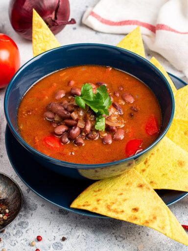 Sopa de frijol servida en un tazón. Lleva totopos de decoración.